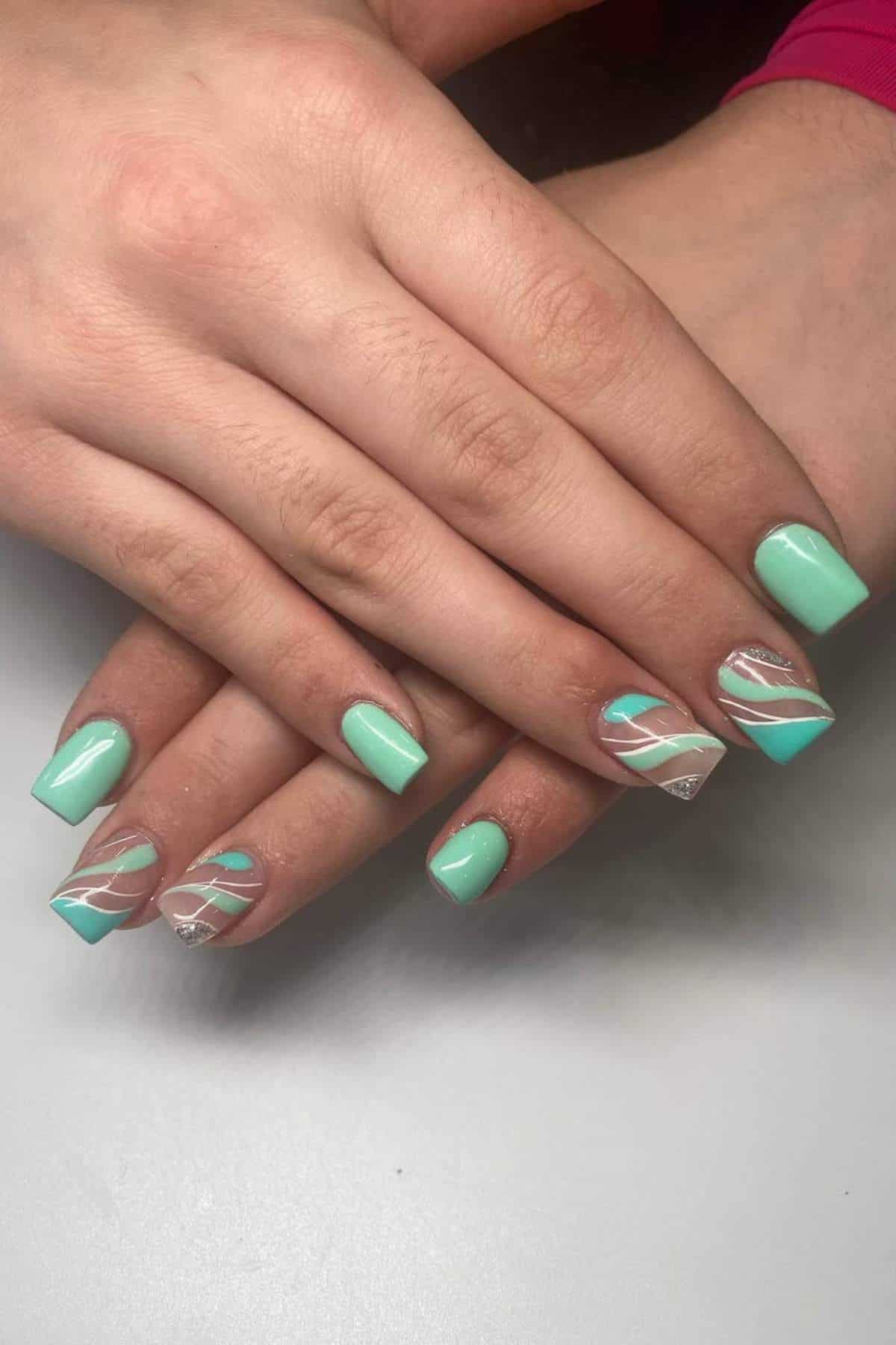 Hands with medium-length, square-shaped nails painted mint green, some featuring clear sections and white wavy line designs.