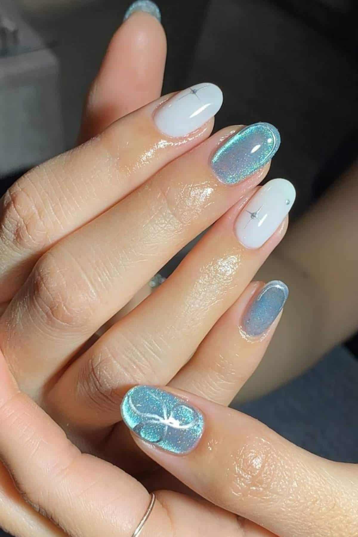 Close-up of a hand with manicured nails featuring a mix of iridescent blue polish and white polish, some with subtle line designs.