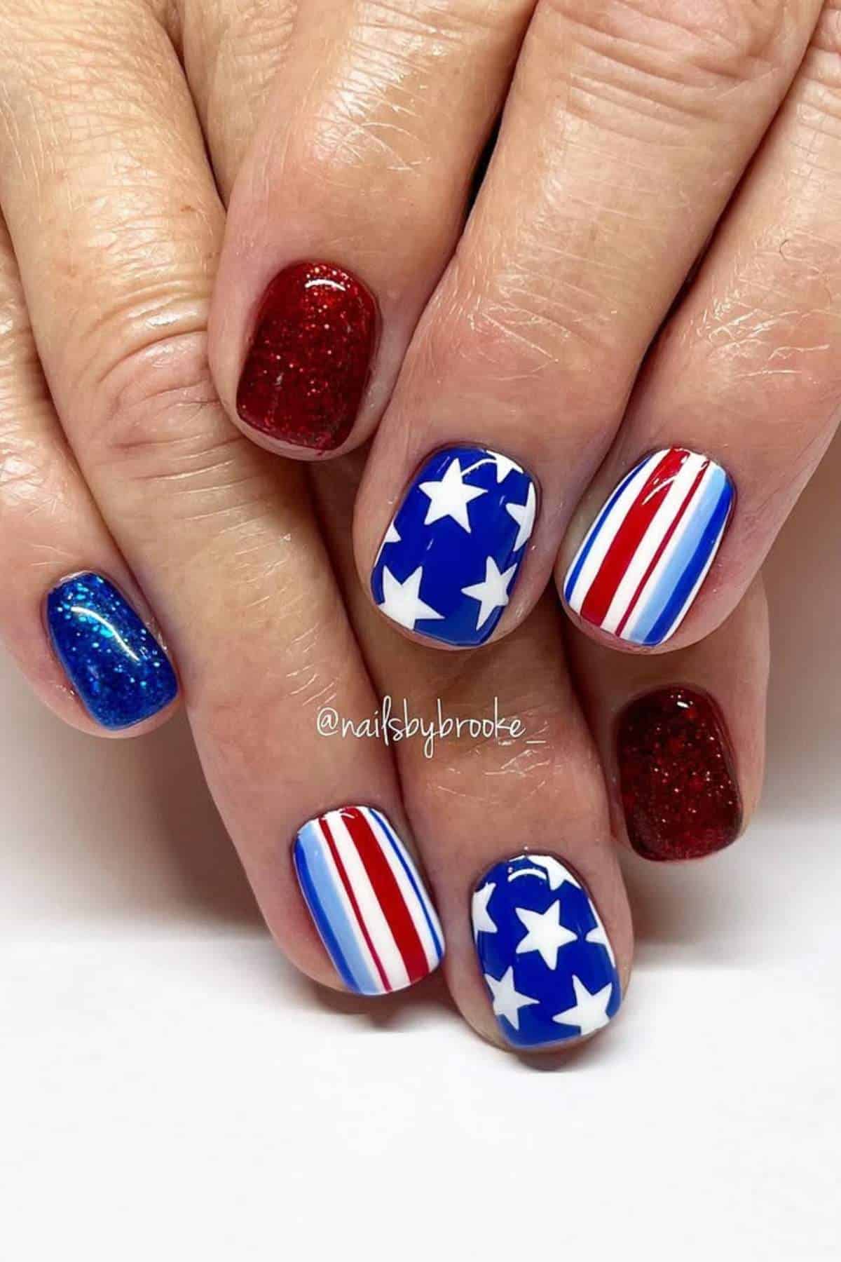 Fingernails painted with red glitter, blue with white stars, and red, white, and blue stripes, inspired by the American flag.
