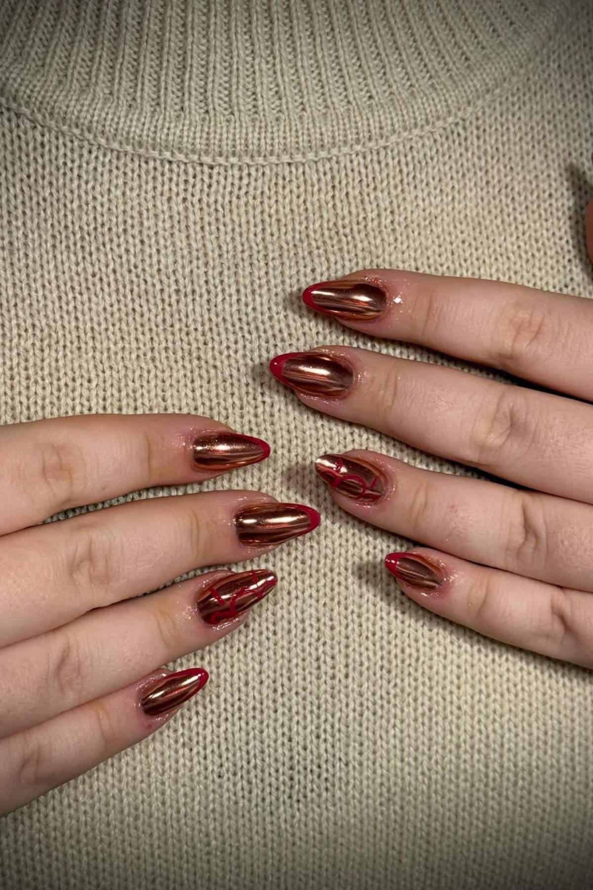 Hands with long, almond-shaped nails featuring a shiny, metallic red polish are placed on a beige knitted sweater.