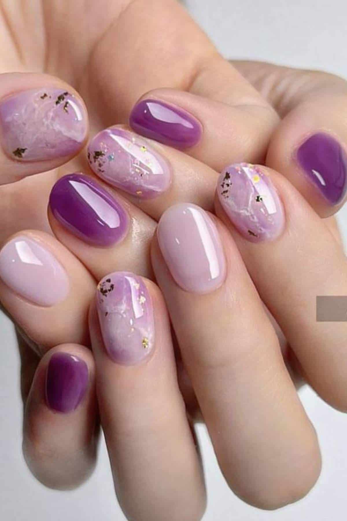 Close-up of hands with manicured nails painted in shades of purple and pink, featuring marble and glitter accent designs.