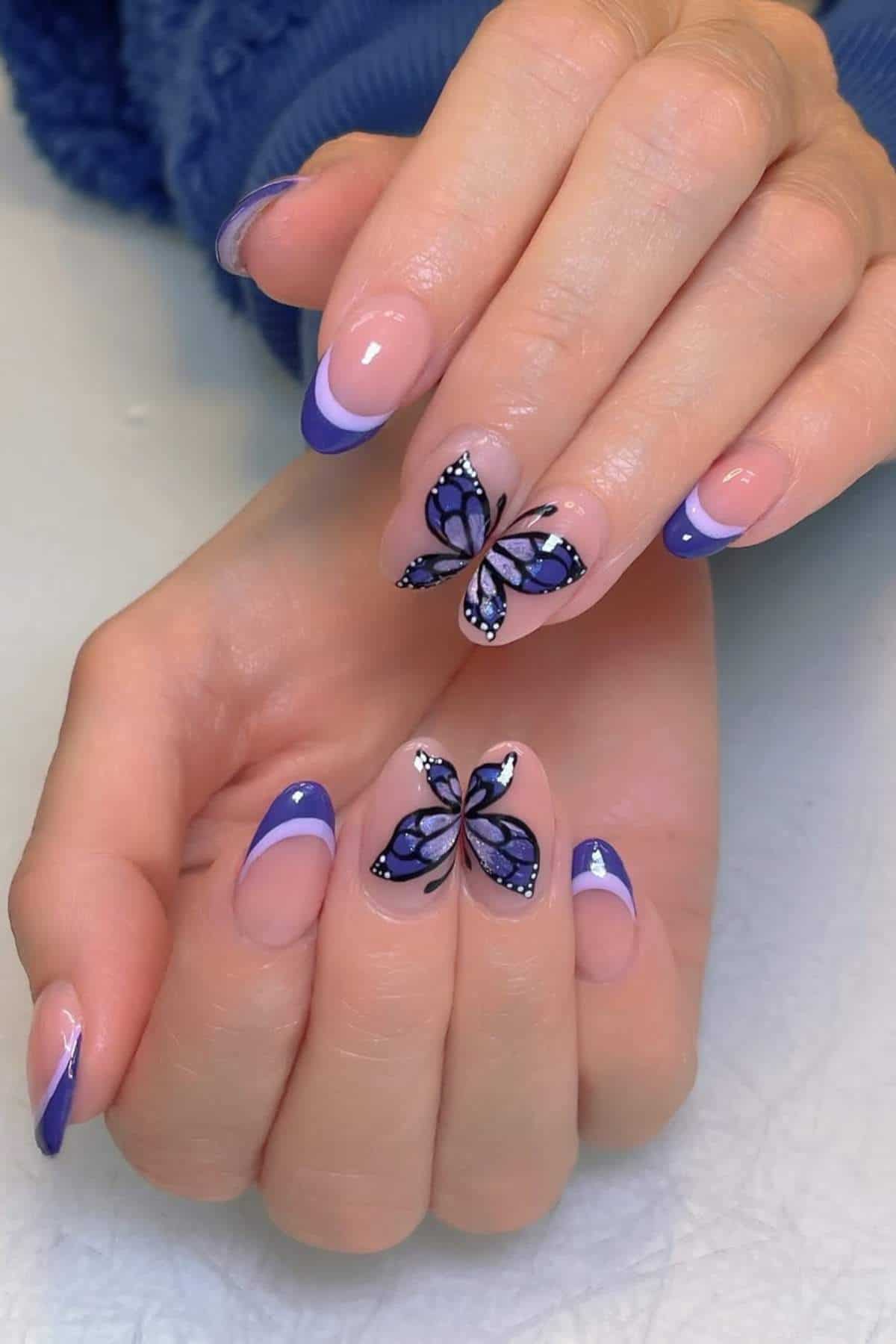 Hands with almond-shaped nails featuring purple French tips and detailed purple butterfly nail art on the middle and ring fingers.