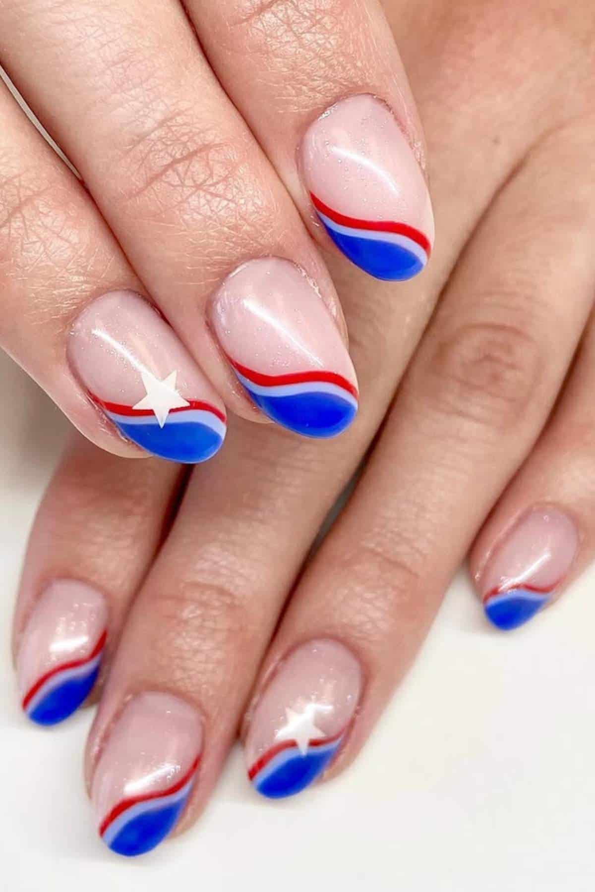 Close-up of hands with nude nails featuring red and blue wavy French tips and small white star accents on the ring fingers.