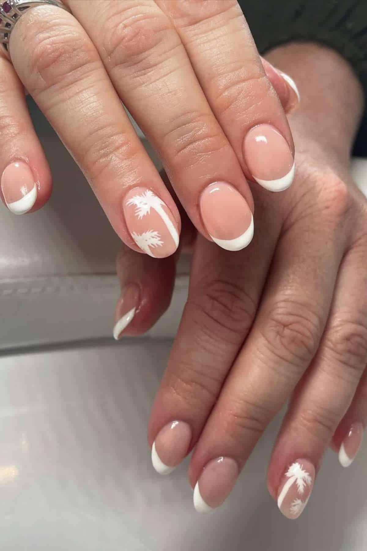 Hands with a French manicure featuring white tips and two accent nails with white palm tree designs.