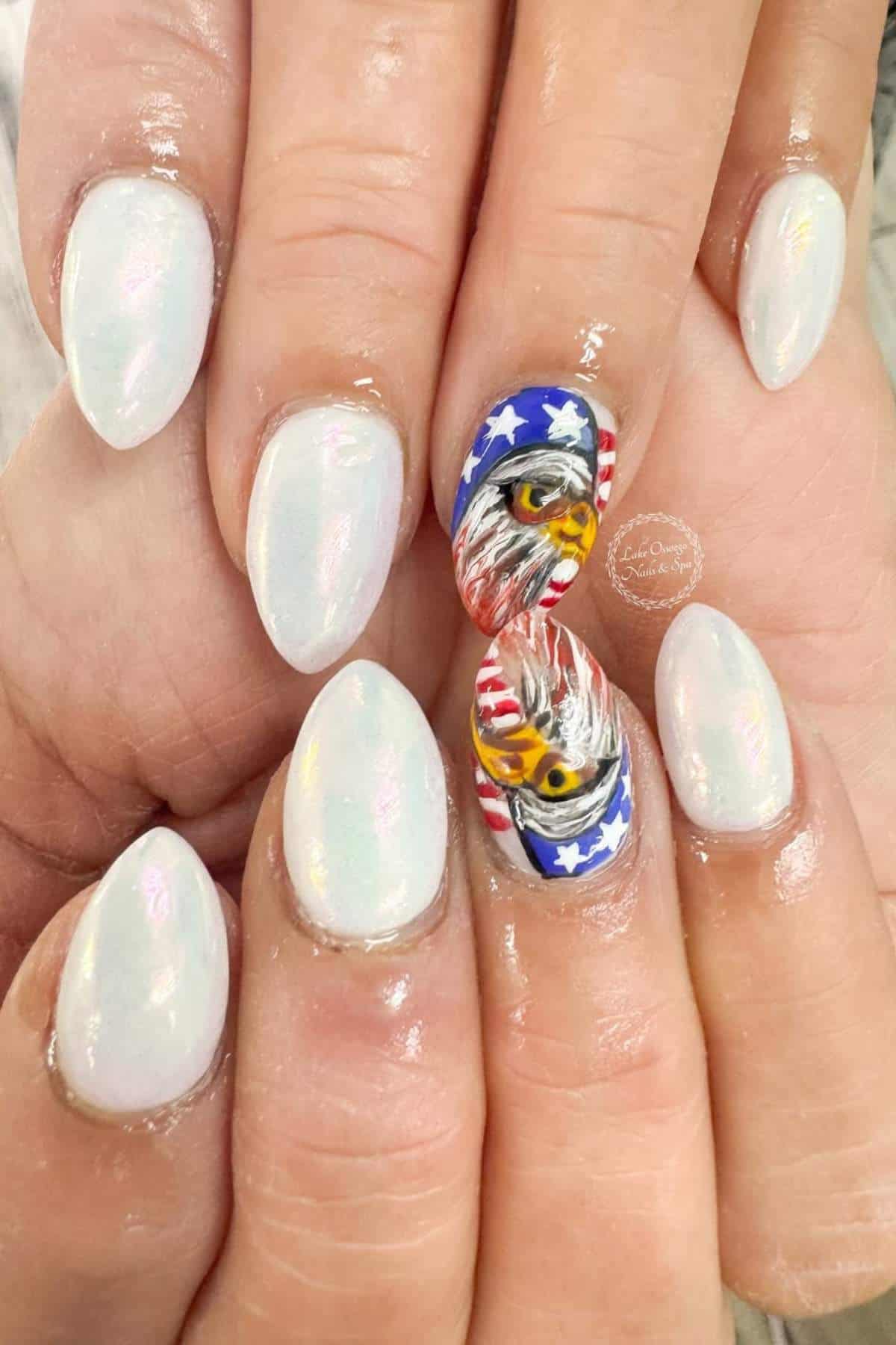 A set of hands with iridescent white nails; the middle nails feature a painted bald eagle and an American flag design.