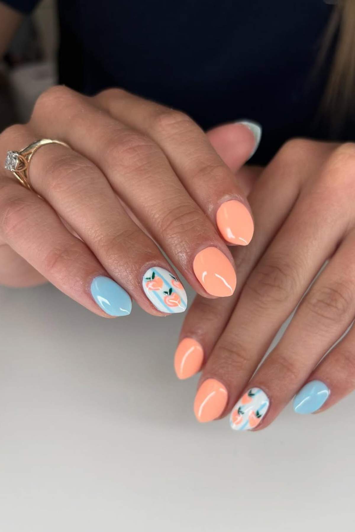 Hands with almond-shaped nails painted in pastel blue and peach, featuring floral designs on two accent nails.