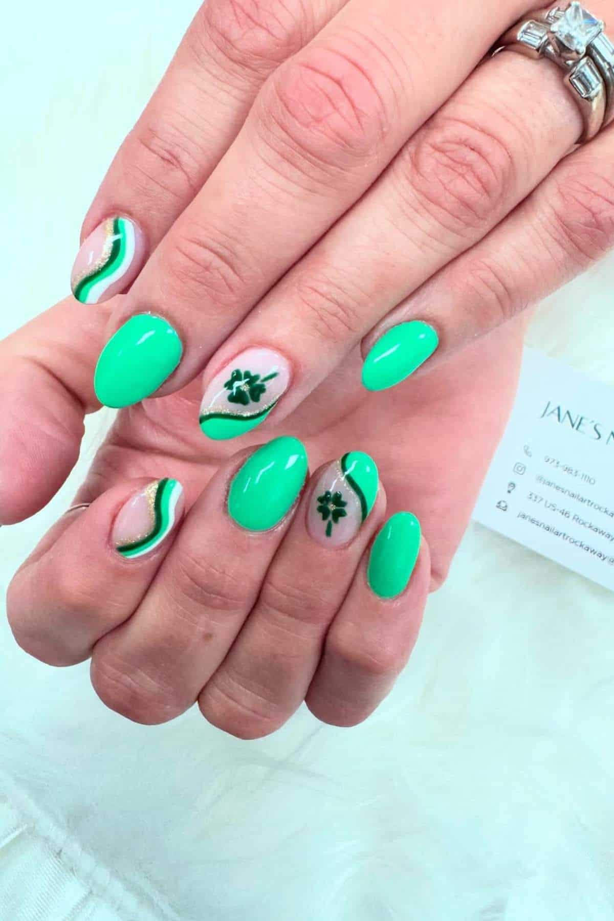 Hands with bright green manicured nails, some featuring clover leaf designs and wavy white and green lines. A diamond ring is visible on one finger.