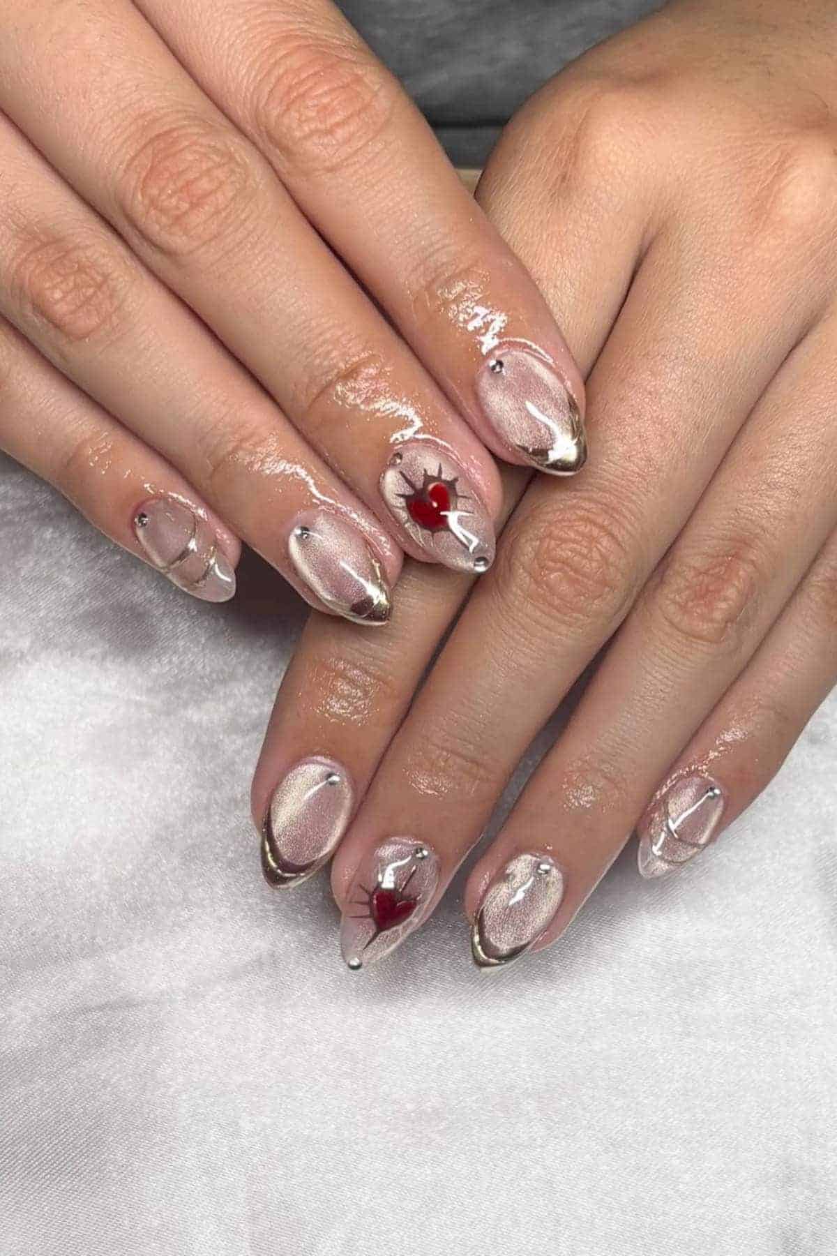 Hands with almond-shaped nails featuring a sheer pink base, silver metallic tips, clear 3D details, and a single red gemstone accent on each middle finger.