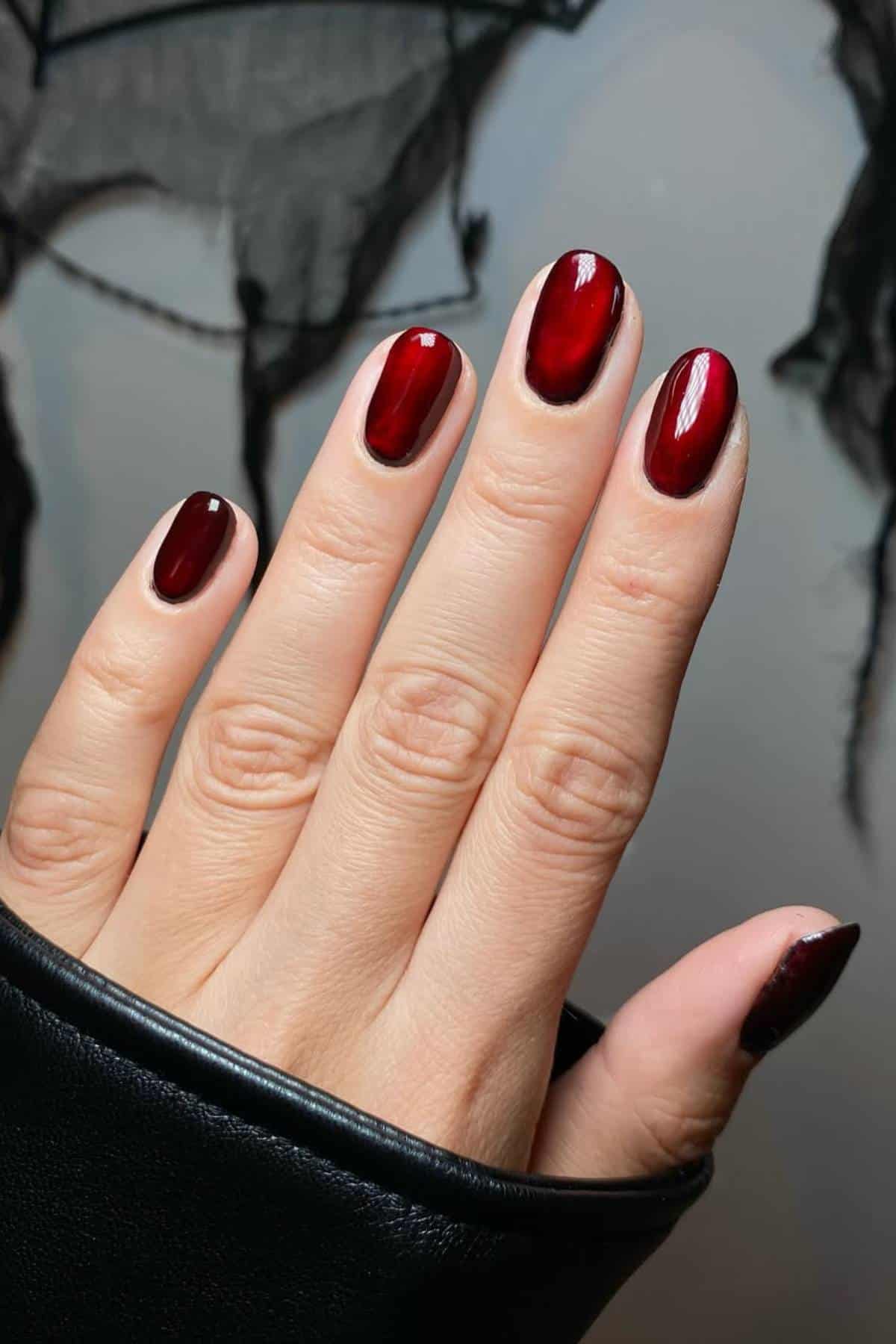 A hand with neatly manicured nails painted in a shiny gradient of deep red to black; the person is wearing a black sleeve.