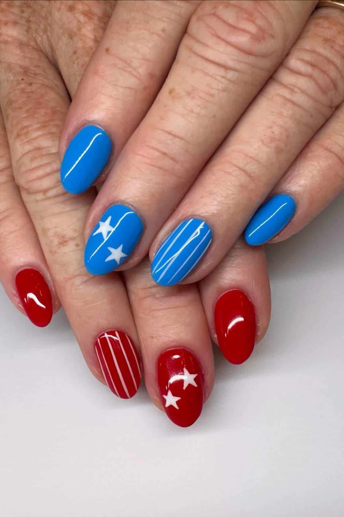 Hands with manicured nails painted red and blue, featuring white stripes and star designs on some nails.