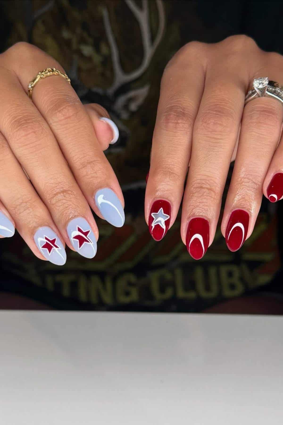 Close-up of hands with manicured nails; left hand features light blue nails with red stars, right hand has red nails with white star and outline designs.