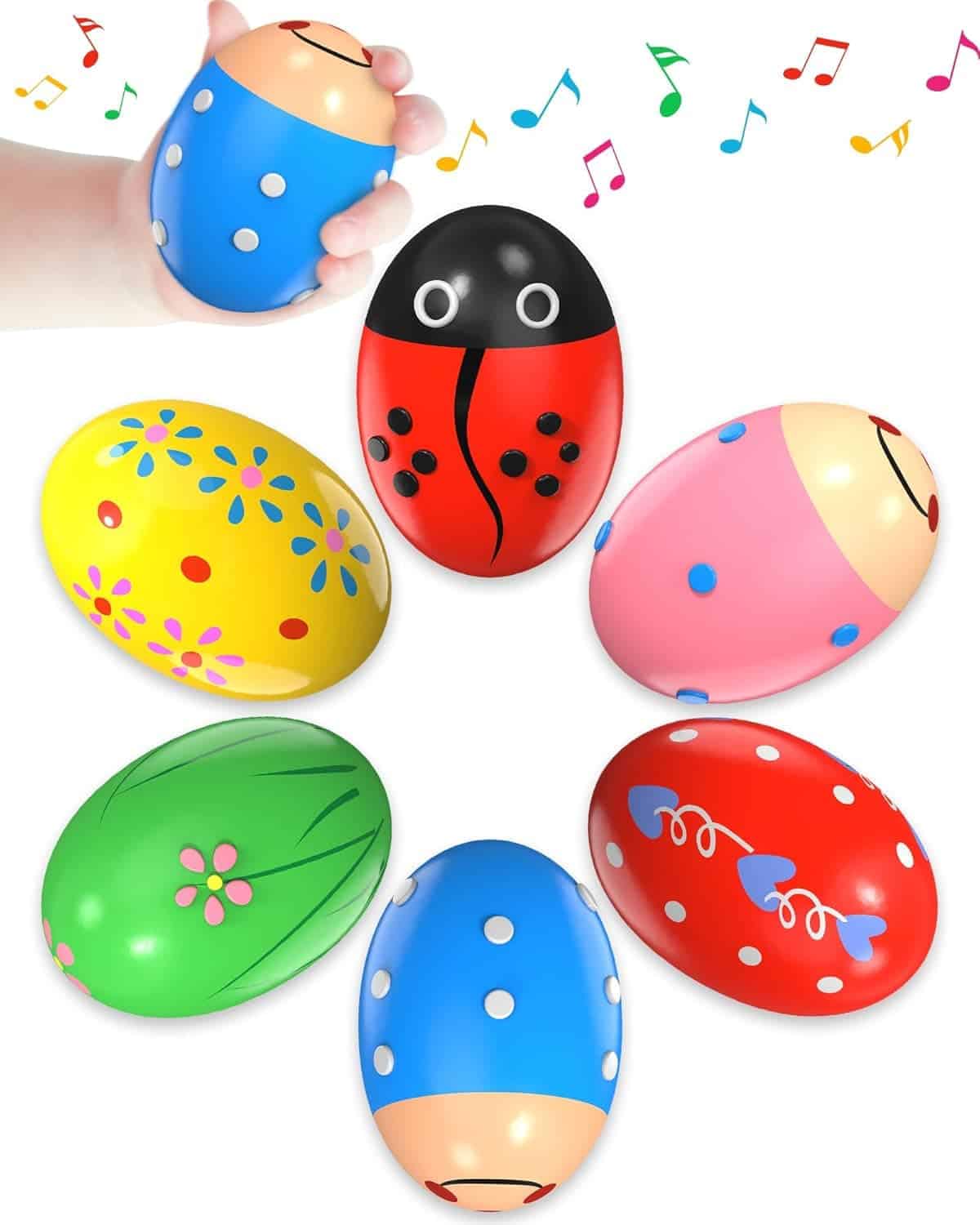 A hand holds a blue maraca egg shaker. Five more colorful, decorated egg shakers are shown below it, with music notes illustrated above.