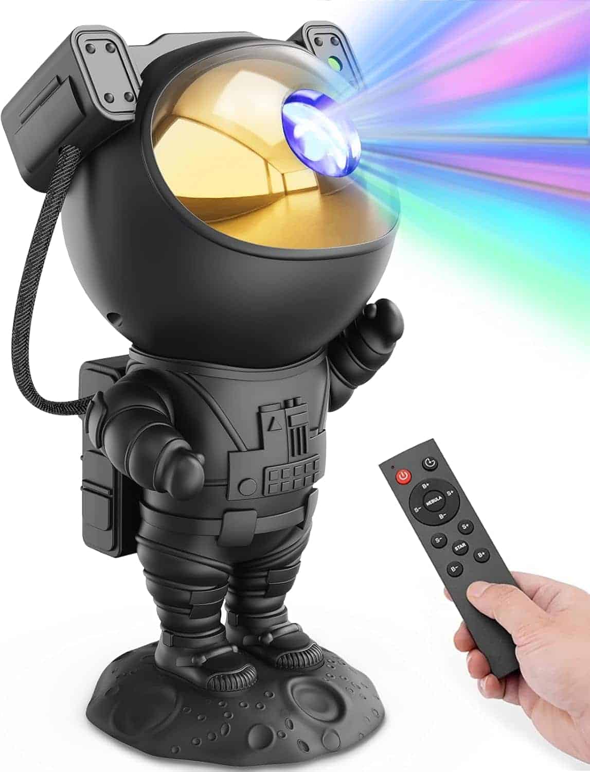A hand holds a remote control aimed at a black astronaut-shaped projector, which emits colorful light beams from its helmet.