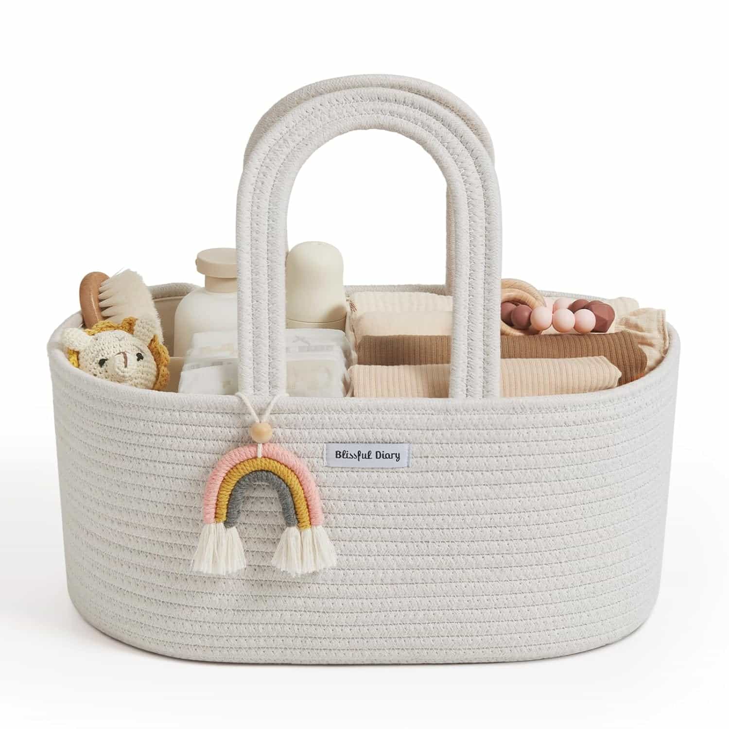 A white woven basket filled with baby items such as bottles, cloths, and toys, with a rainbow charm hanging on the handle.