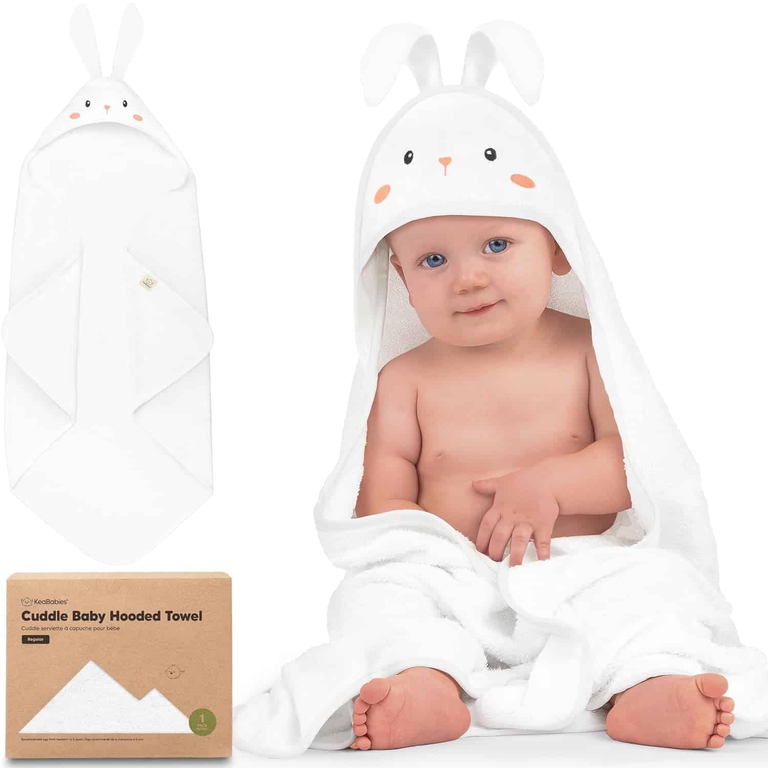 A baby sits wrapped in a white hooded towel with bunny ears and face. Next to the baby are the folded towel and product packaging labeled "Cuddle Baby Hooded Towel.