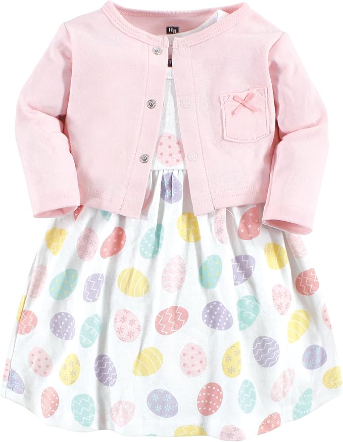 Pink baby cardigan with a front pocket over a white dress featuring a colorful pastel Easter egg pattern.