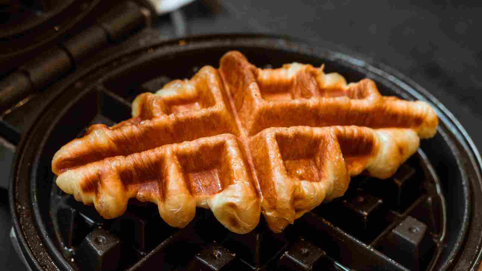 A golden brown waffle sits on an open waffle iron, ready to be removed.