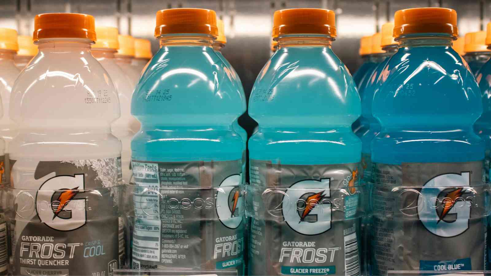 Several bottles of blue and clear Gatorade Frost sports drinks are lined up on a refrigerated store shelf.