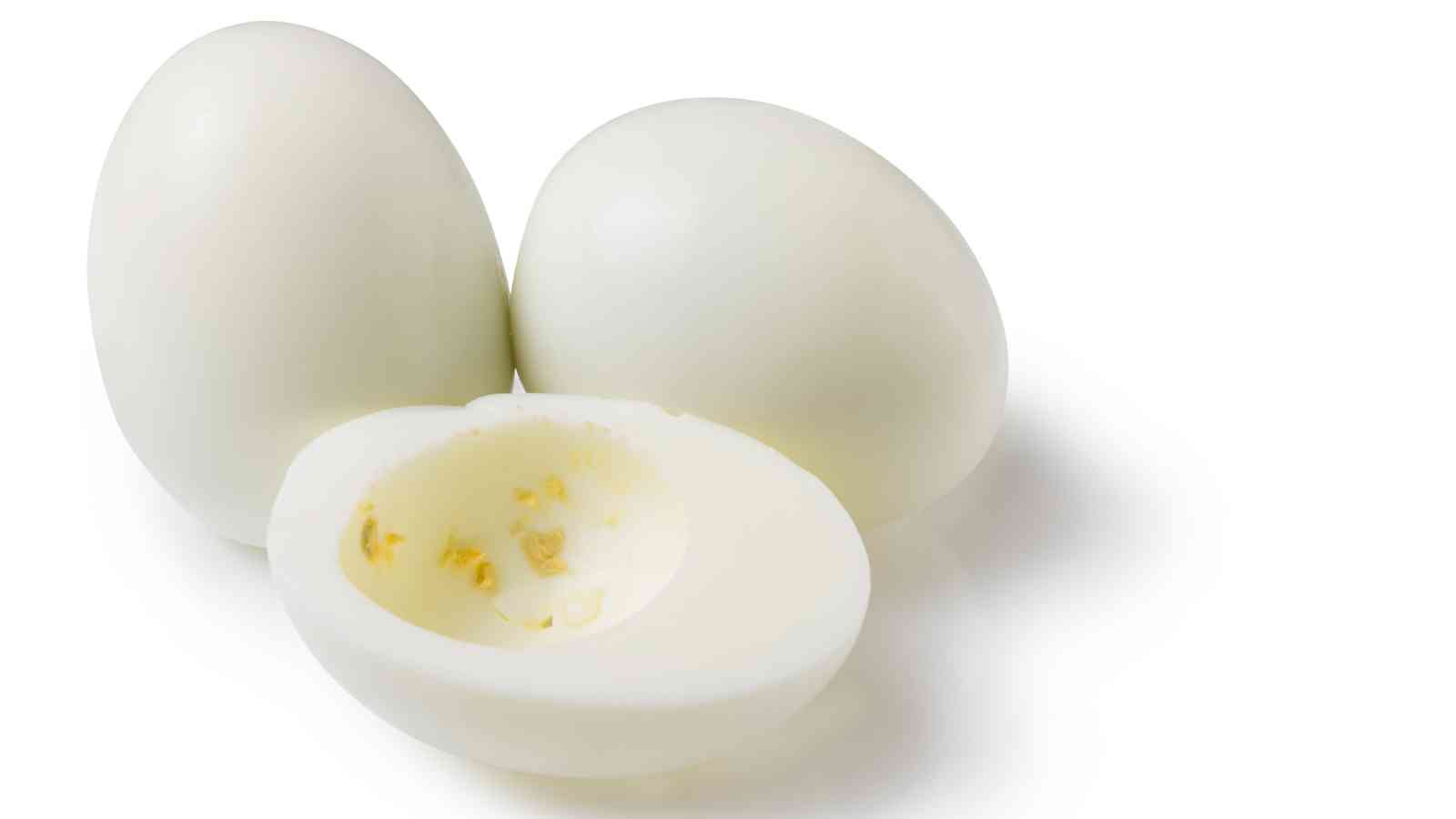 Three hard-boiled eggs, two whole and one sliced in half with the yolk removed, on a white background.