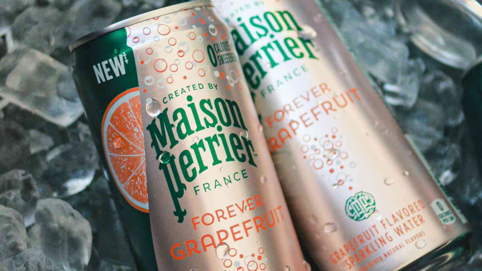 Two cans of Maison Perrier Forever Grapefruit sparkling water rest on ice, condensation visible on the cans.