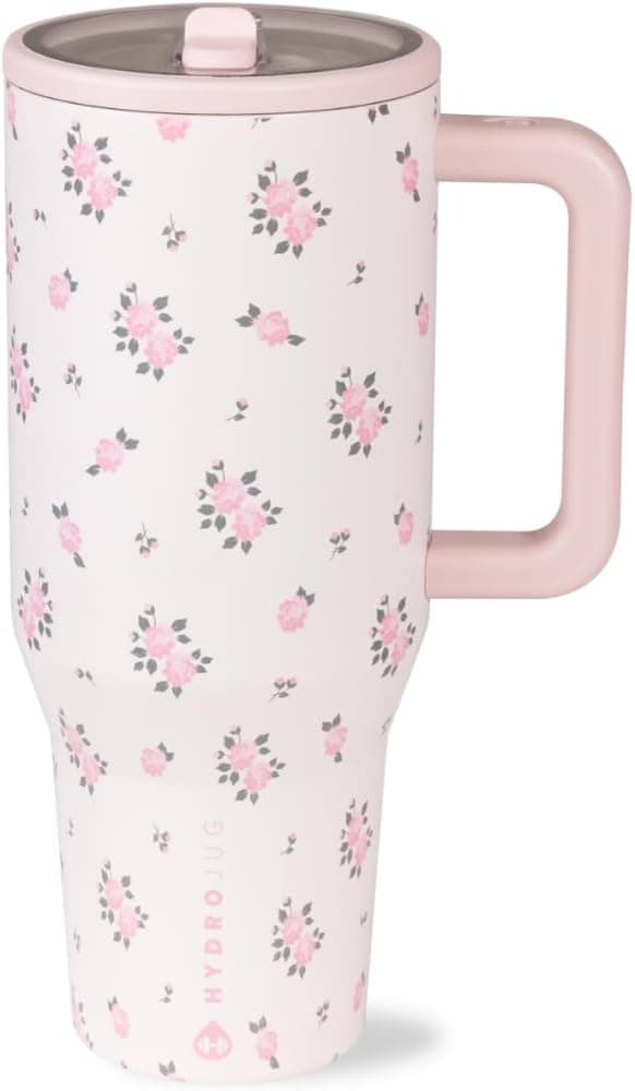 A tall, pink travel mug with a handle, featuring a pattern of small pink flowers and a clear lid.