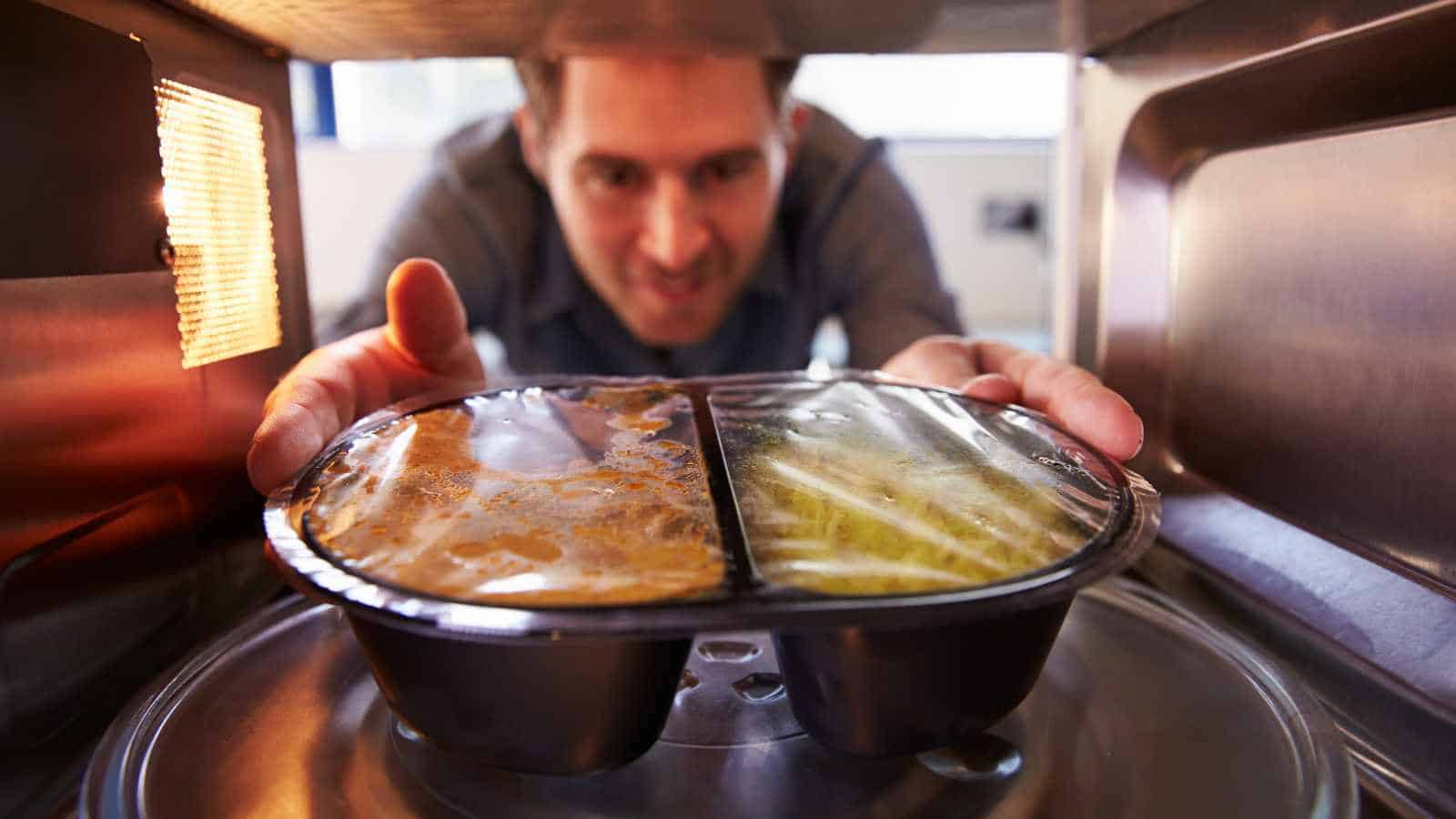 A person places a plastic tray of packaged microwave meal inside a microwave oven, preparing to heat the food.