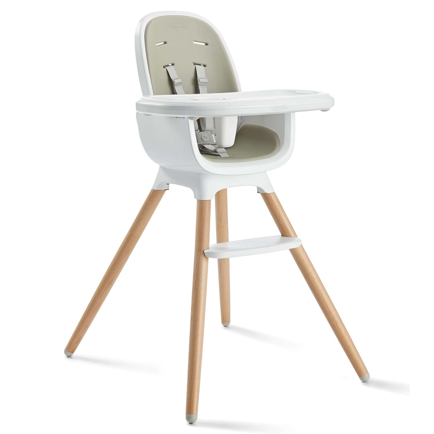 Modern baby high chair with light wooden legs, a white plastic seat, grey harness, a footrest, and a detachable tray.