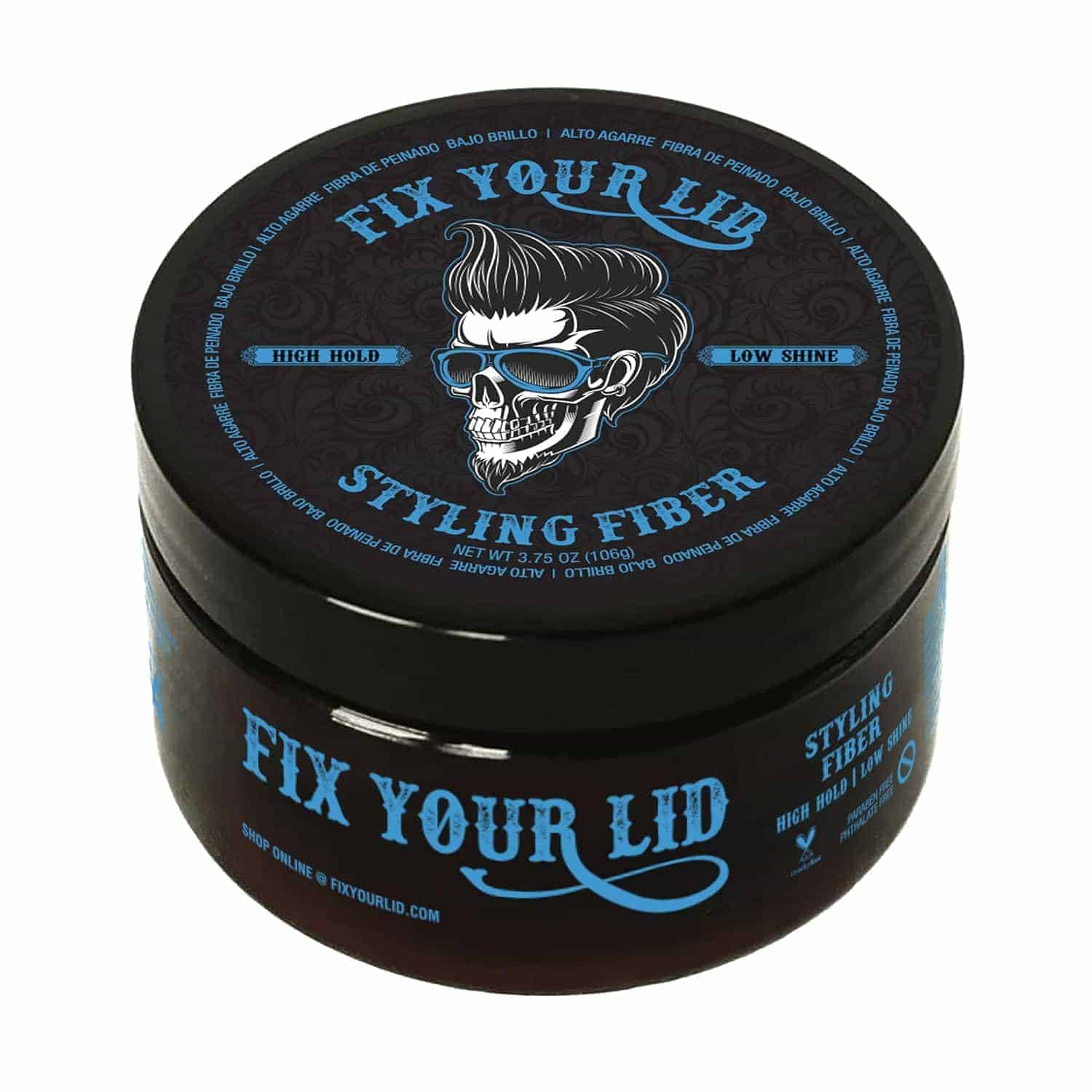 A round container of Fix Your Lid Styling Fiber with a skull illustration wearing sunglasses and styled hair on the lid, labeled high hold and low shine.