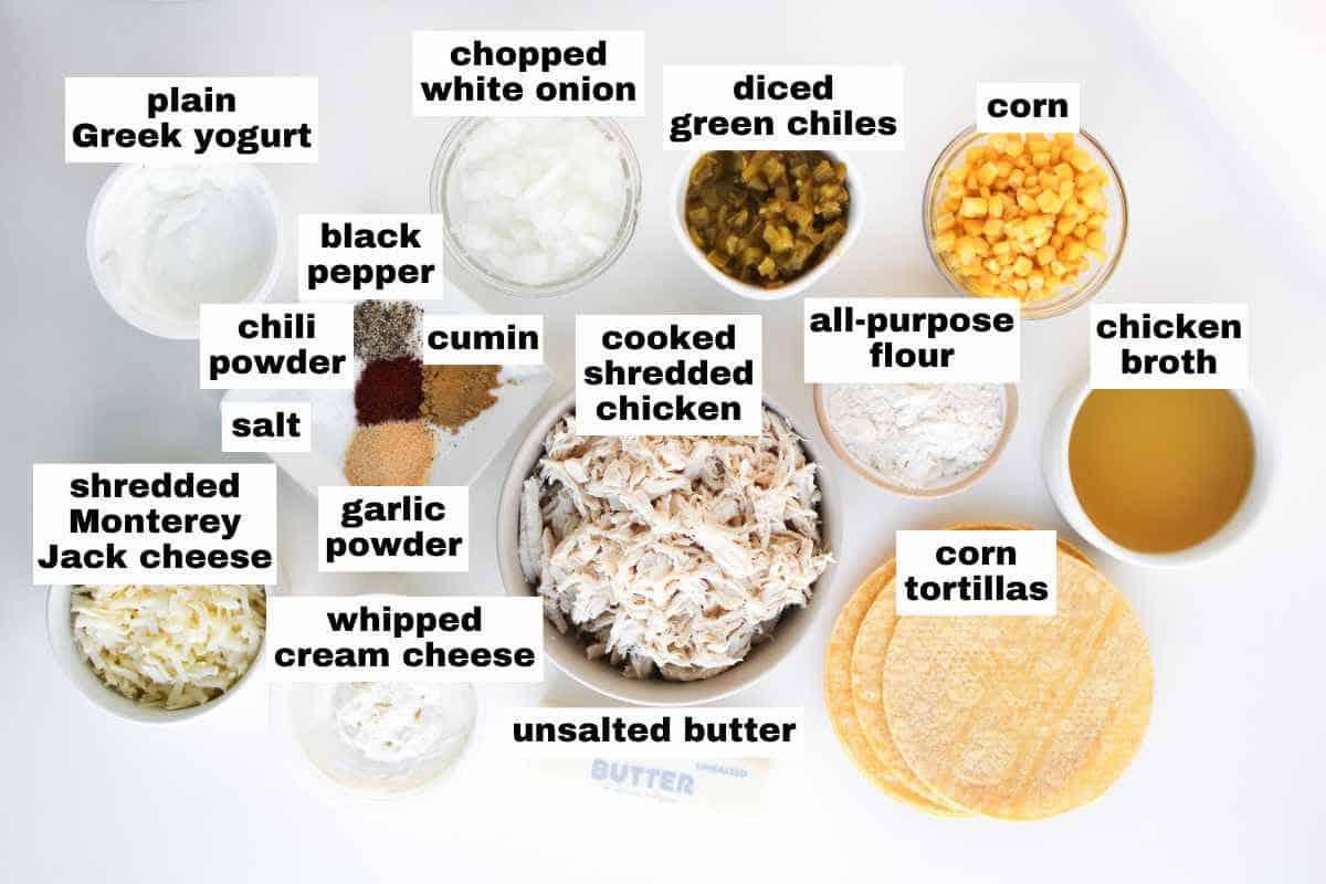 Top-down view of labeled ingredients for a chicken enchilada recipe, including shredded chicken, corn, tortillas, cheese, Greek yogurt, spices, broth, and more.