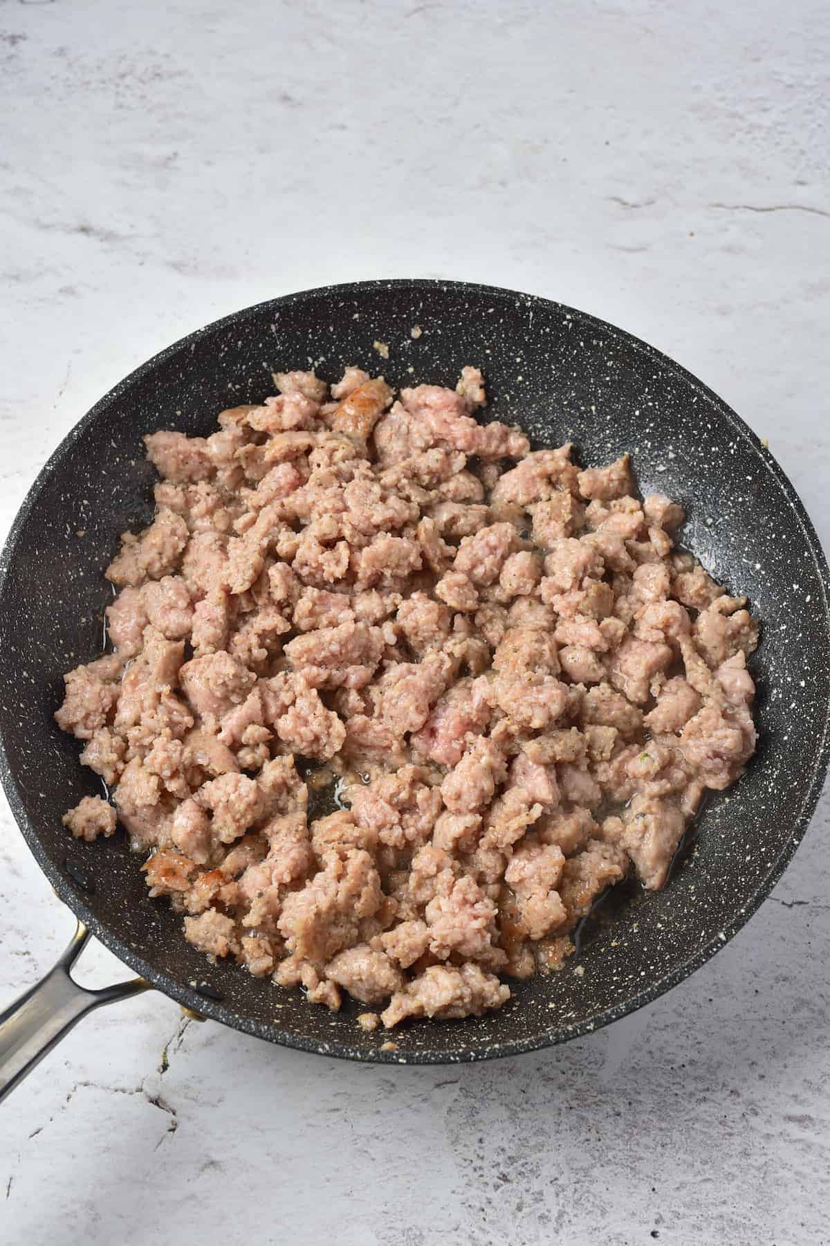 Ground meat cooking in a black nonstick skillet on a light-colored surface.
