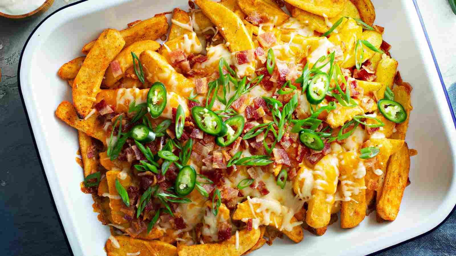 A tray of seasoned fries topped with melted cheese, bacon bits, sliced jalapeños, and chopped green onions.