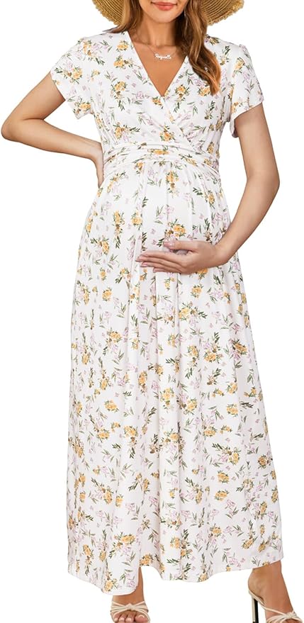 Woman in a floral print maxi dress and sun hat, holding her pregnant belly with one hand and her hat with the other.