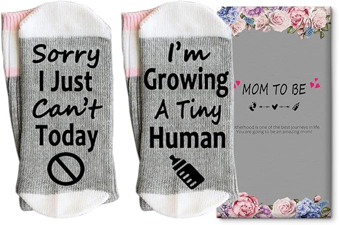 A pair of gray socks with white tops read "Sorry I Just Can't Today" and "I'm Growing A Tiny Human" beside a floral "Mom To Be" card.
