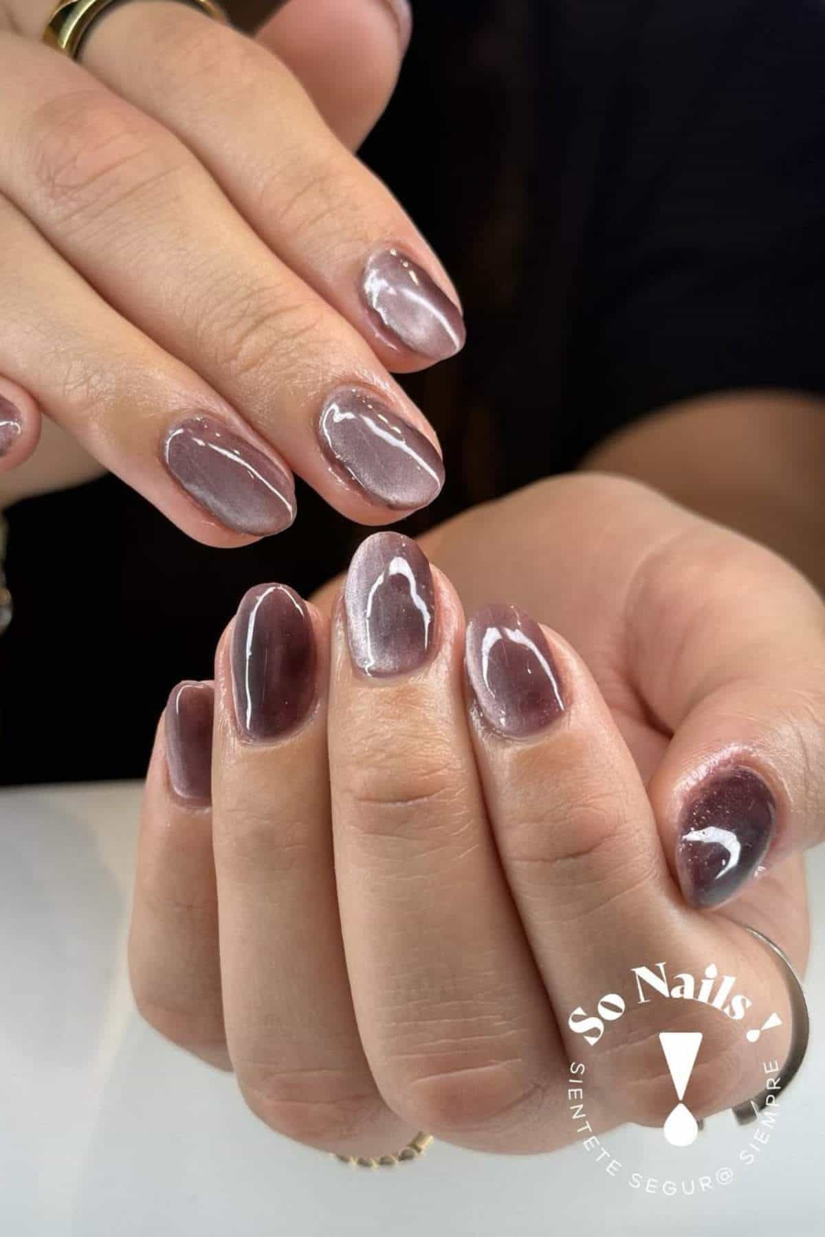 Close-up of hands showing short, oval-shaped nails with glossy, marbled brown and nude nail art. "So Nails" logo is visible in the bottom right corner.