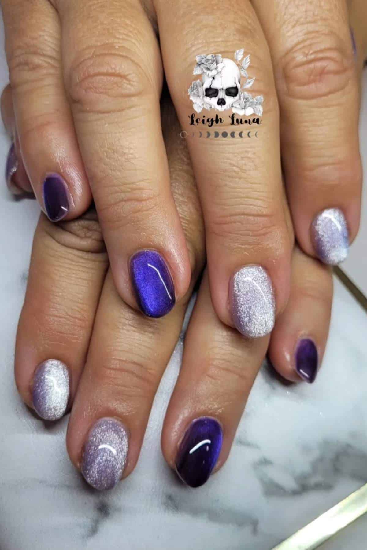 Hands with short, oval-shaped nails painted in alternating shades of shimmery purple and silver, displayed on a white marble surface.