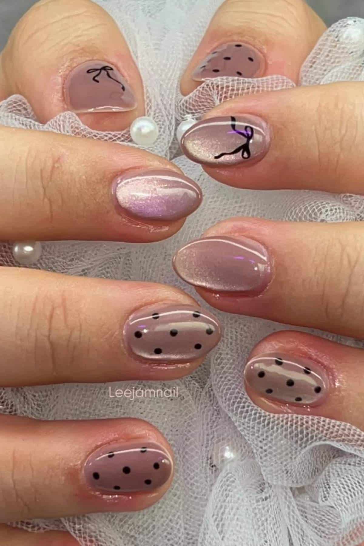 Hands with short nails painted in light pink and nude shades, featuring black dots, abstract lines, and glossy finishes, resting on white mesh fabric.
