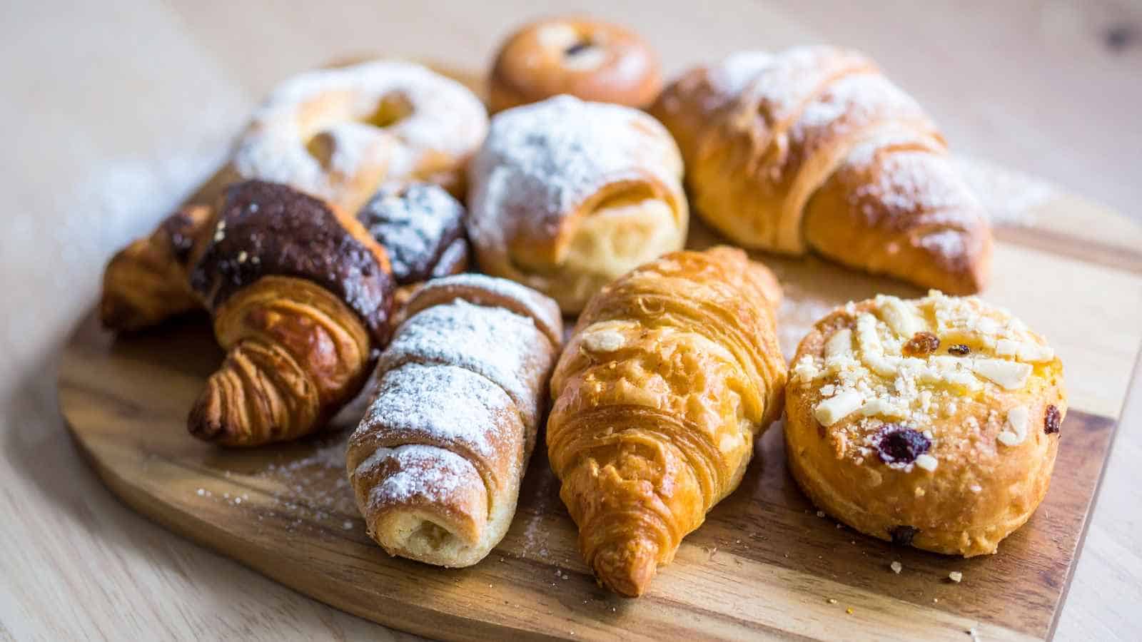 An assortment of croissants and pastries dusted with powdered sugar arranged on a wooden serving board.