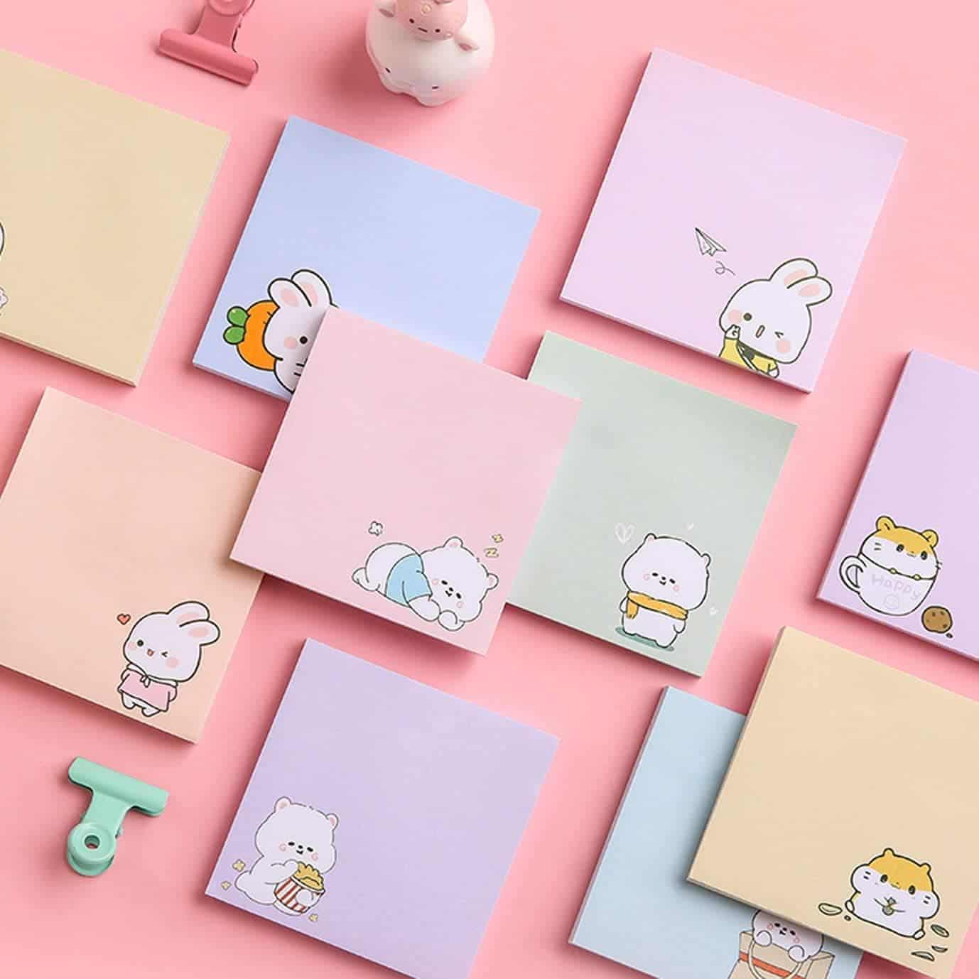 A variety of pastel sticky notes featuring cute cartoon animals, arranged neatly on a pink background with clips and a cat figurine.