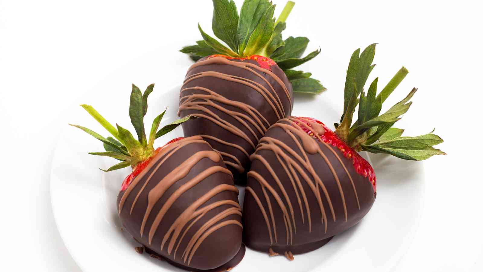 Three strawberries dipped in dark chocolate and drizzled with milk chocolate are arranged on a white plate.