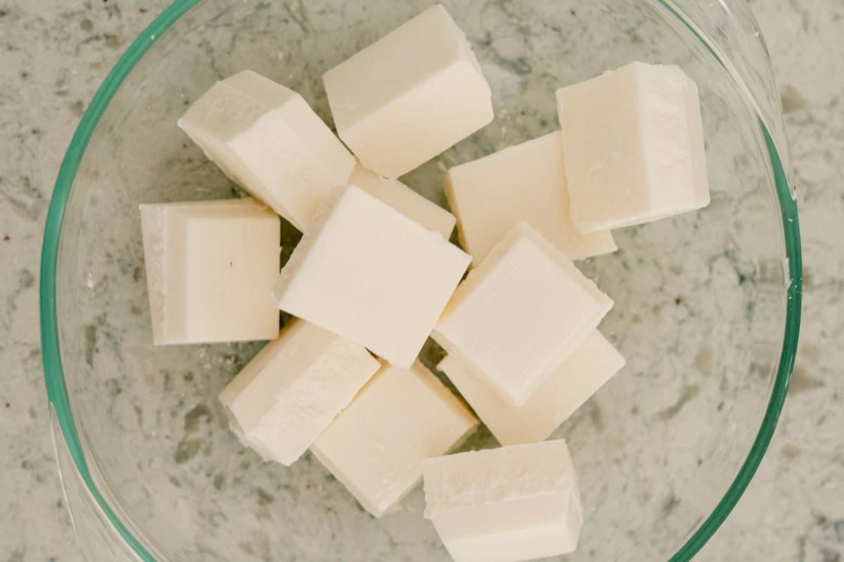 A glass bowl containing several square cubes of solid white butter on a speckled countertop.