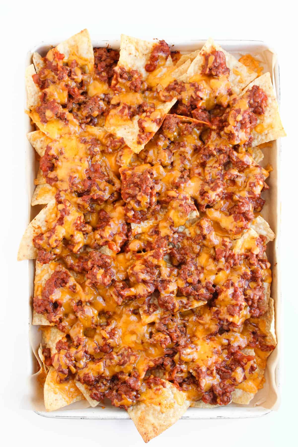 A tray of nachos topped with melted cheese and seasoned ground beef on a white background.