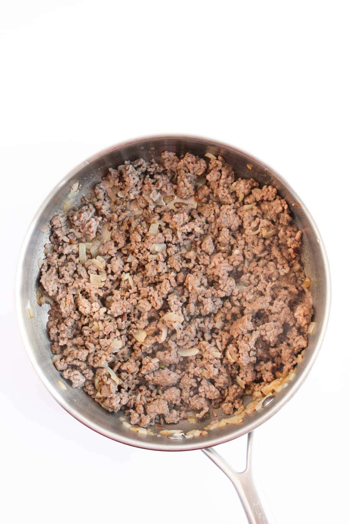 Cooked ground beef with diced onions in a stainless steel skillet, viewed from above on a white background.