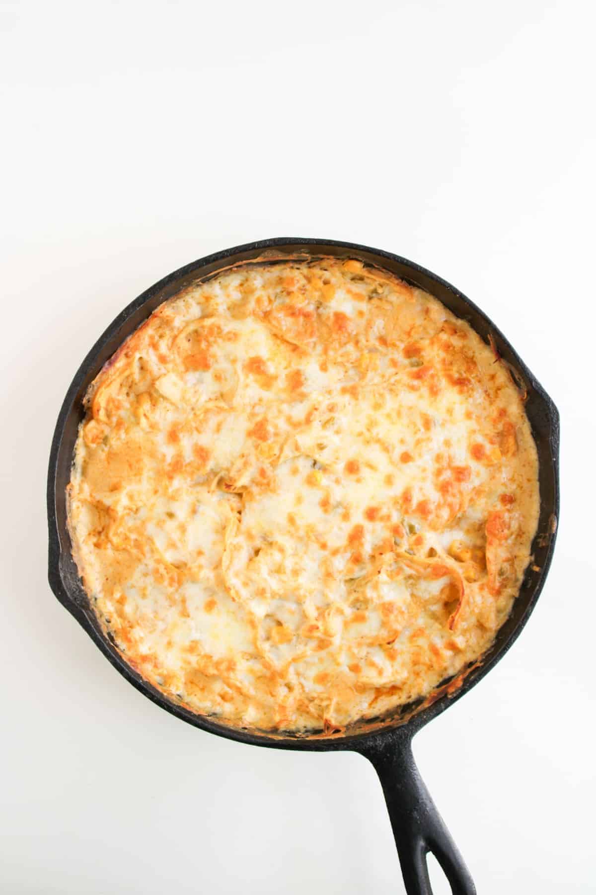 A black cast iron skillet filled with a baked, cheesy skillet featuring a golden-brown melted cheese topping.
