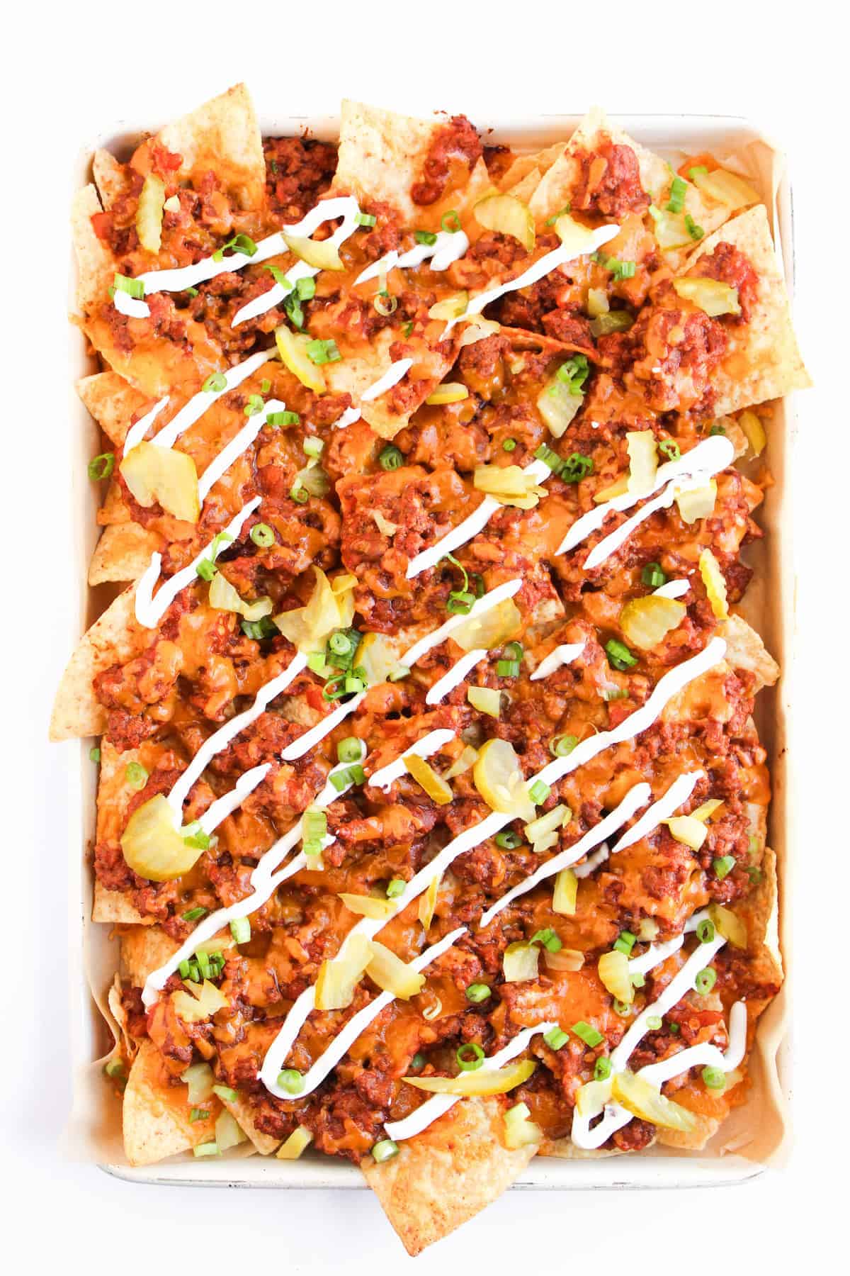 A tray of nachos topped with ground meat, melted cheese, chopped green onions, diced tomatoes, and drizzled with sour cream.