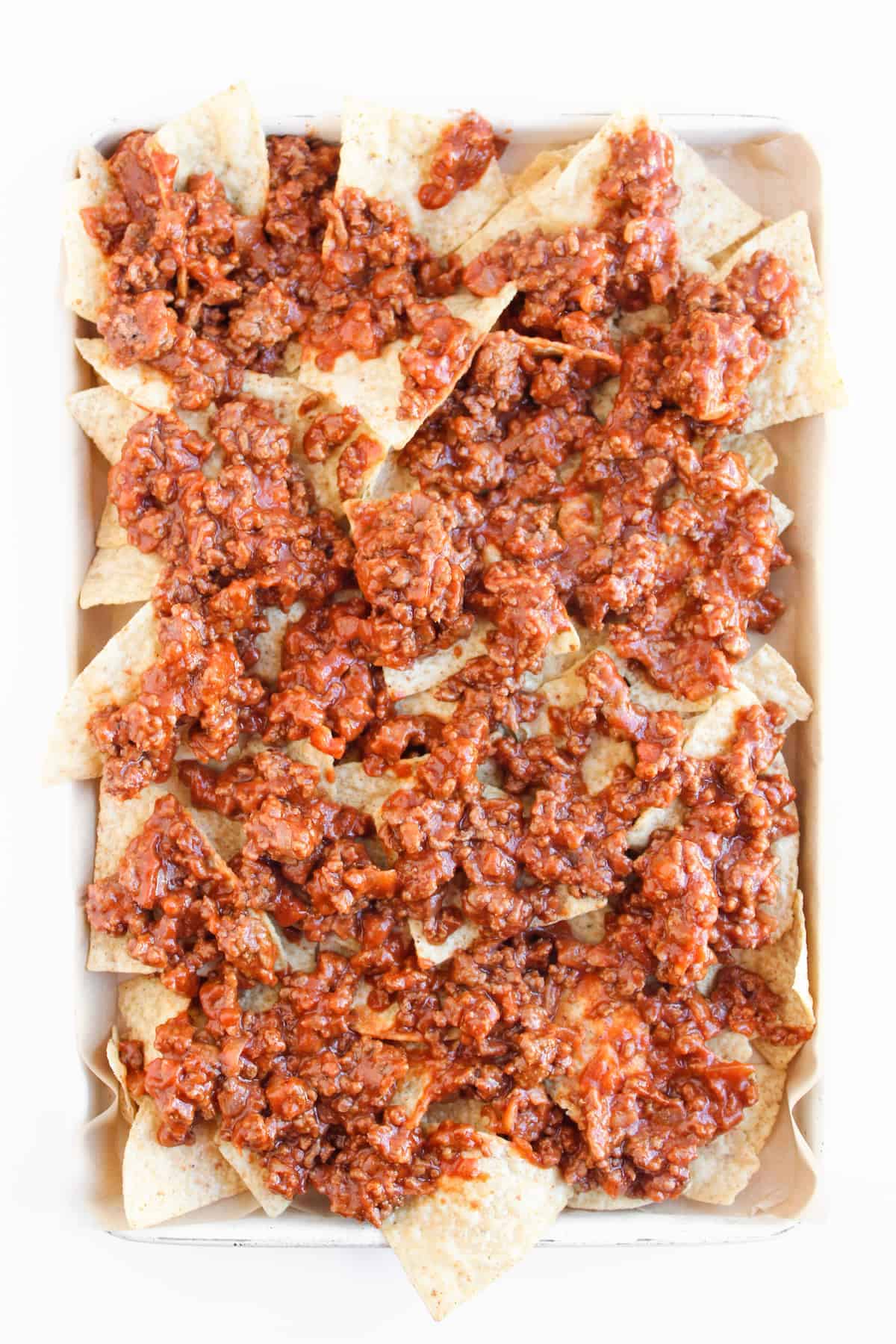 A baking dish filled with tortilla chips topped with seasoned ground beef in a red sauce.