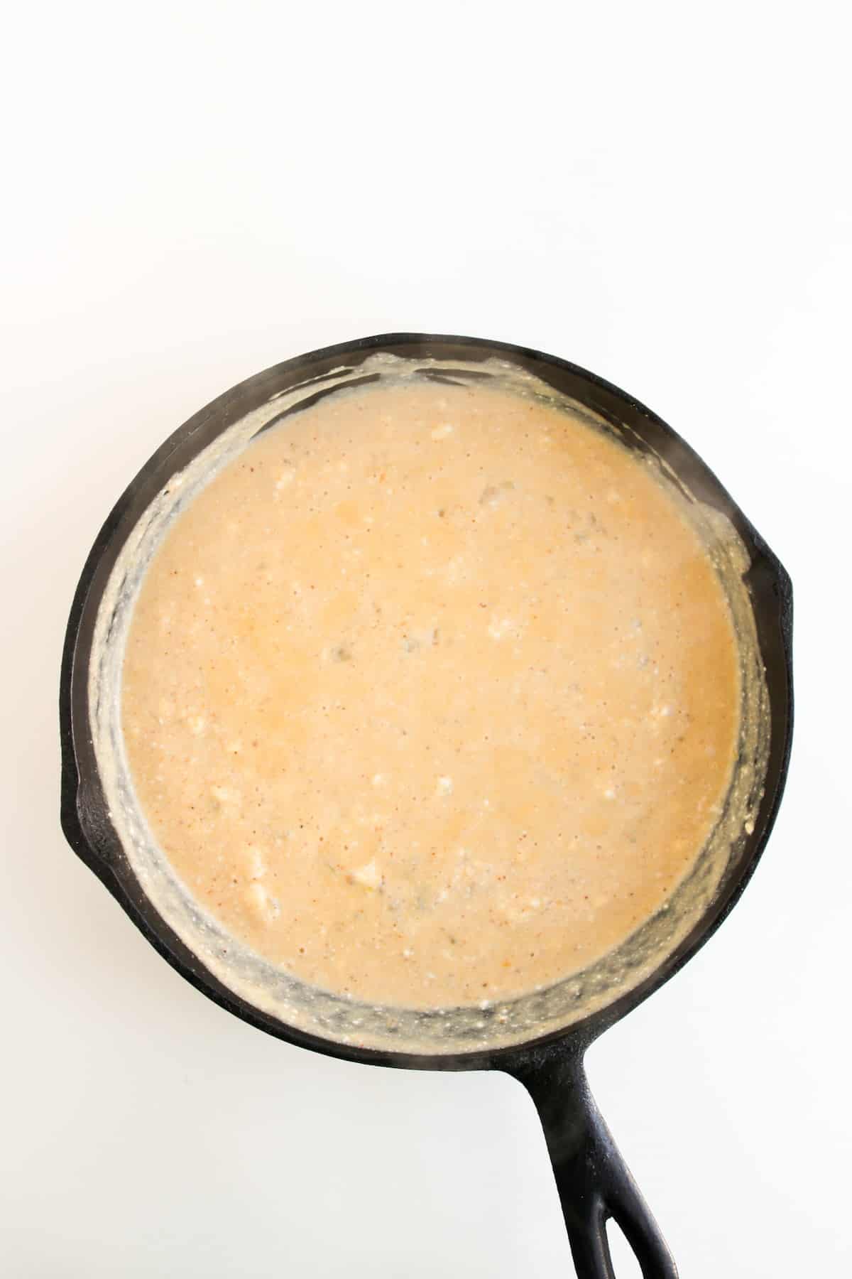 A cast iron skillet filled with a creamy, light orange sauce sits on a white surface.