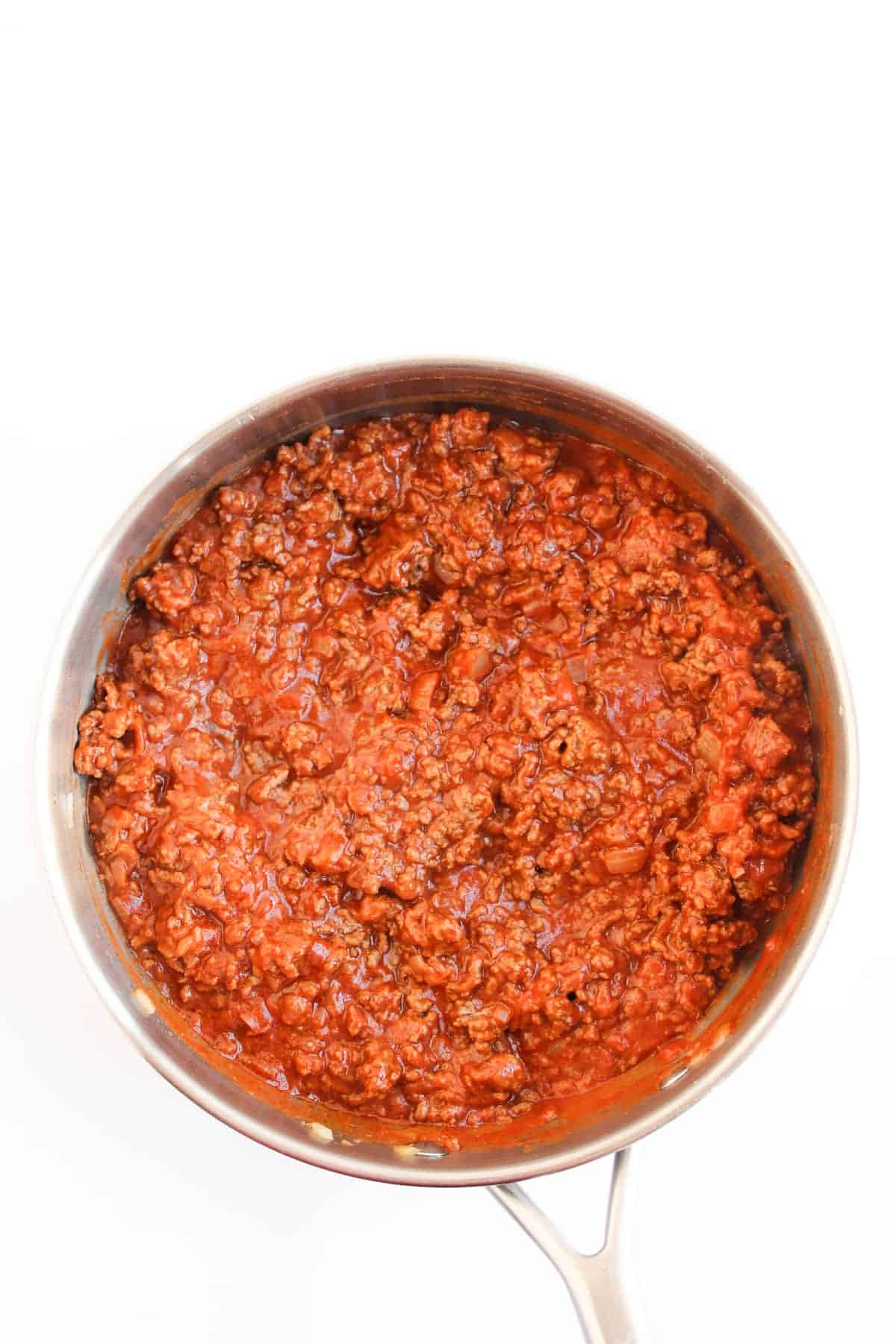 A stainless steel pan filled with cooked ground beef in red tomato sauce, viewed from above on a white background.