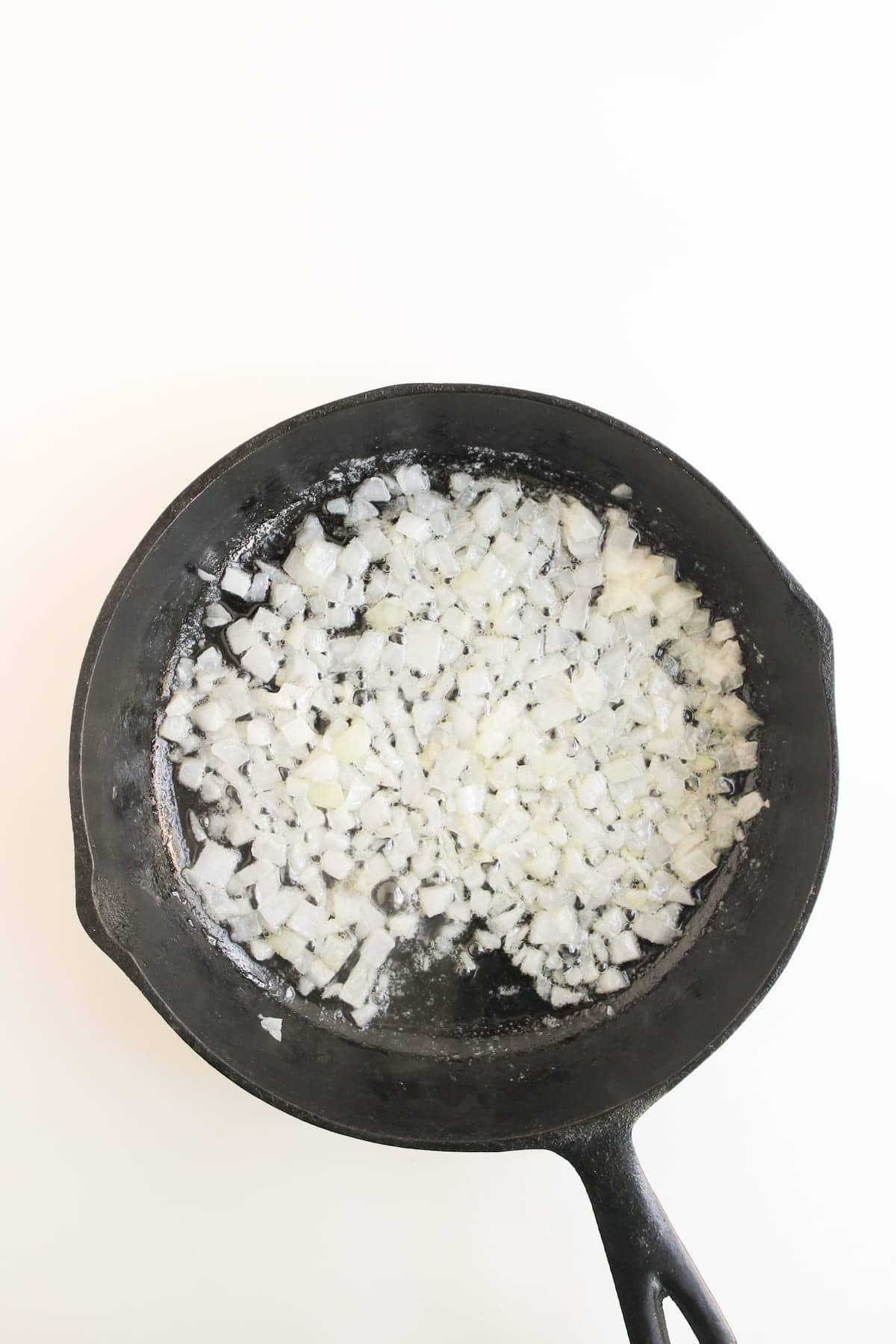 Chopped onions cooking in a black cast iron skillet on a white background.