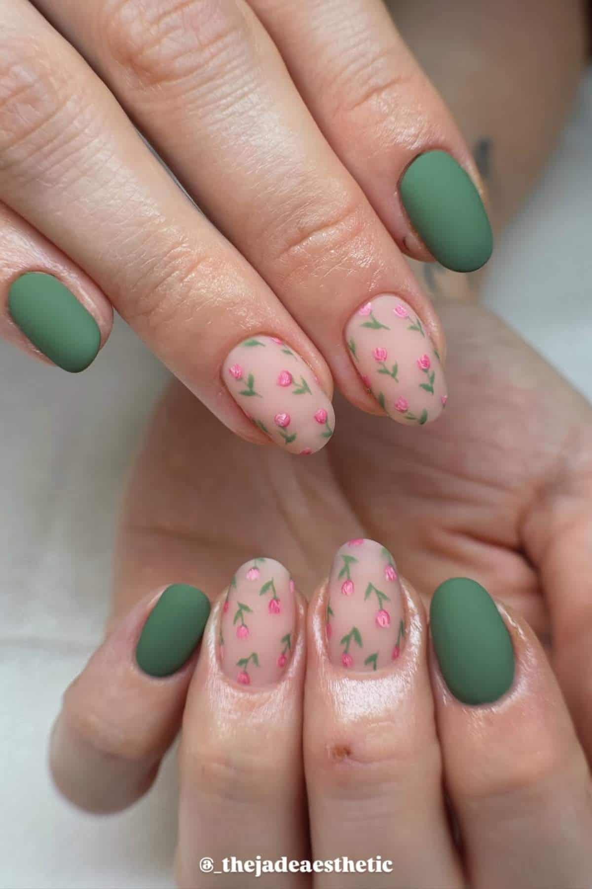 Hands with oval-shaped nails featuring a green matte polish on some fingers and small pink rose designs with green stems on a nude base on others.