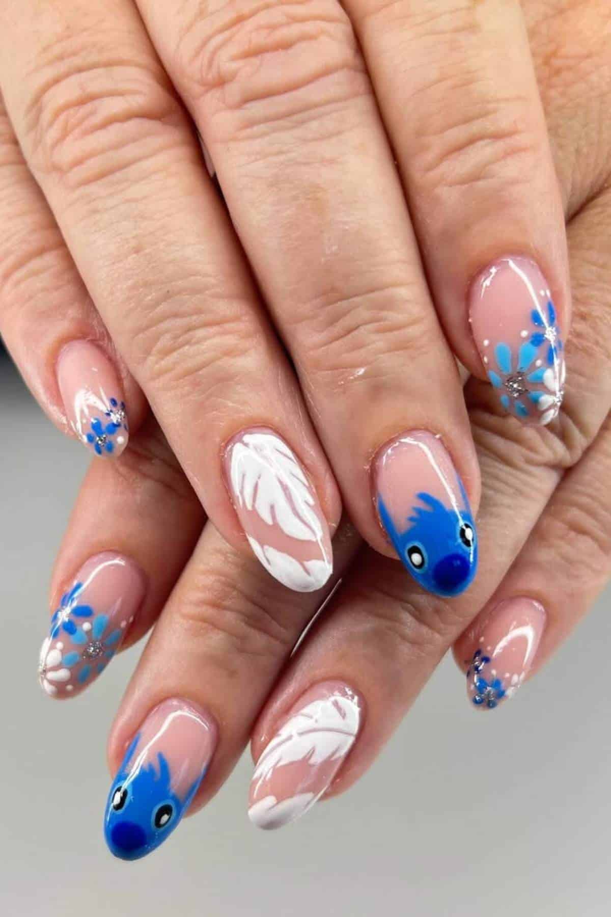 Hands with manicured nails featuring blue and white floral designs, white feathers, and two nails with blue bird faces on a light pink base.